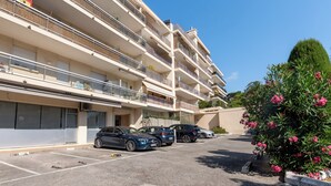 Ein mehrgeschossiges Wohngebäude mit Balkonen, einem Parkplatz mit Autos und einem gepflegten Garten mit blühenden Pflanzen.