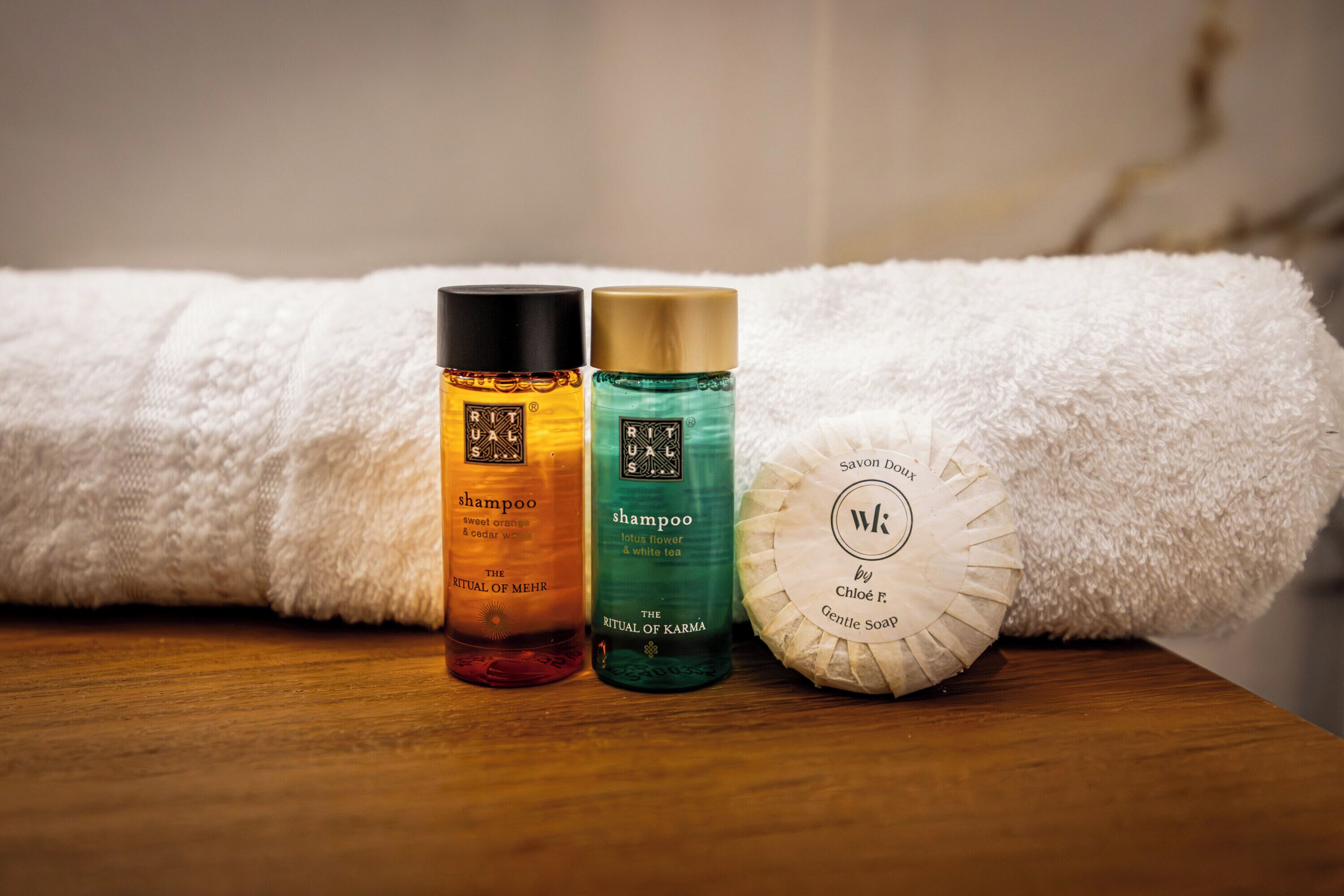 Tre shampoo flasker og en sæbe på en træoverflade med et hvidt håndklæde i baggrunden.