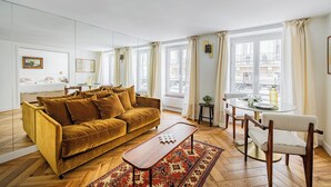 A living room with a sofa, a coffee table, a dining table with chairs, and large windows with curtains. - Le Nid Doré Parisien - Welkeys (Paris)
