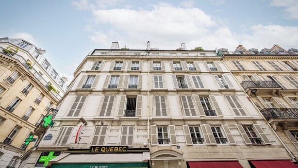 A multi-story building with a prominent pharmacy sign, classical architecture, and a clear sky. - Le Nid Doré Parisien - Welkeys (Paris)