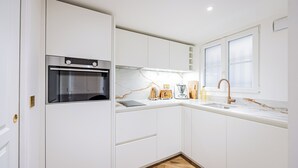 A compact kitchen with white cabinetry, a built-in oven, a window, and a herringbone-patterned wooden floor. - Le Nid Doré Parisien - Welkeys (Paris)