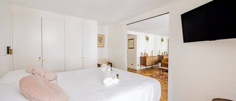 Une chambre d’hôtel avec un lit, un téléviseur fixé au mur et une salle de bain visible à travers une porte ouverte.