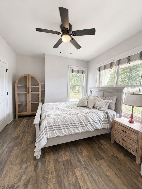 A bedroom with a bed, a ceiling fan, a wardrobe, and a window with blinds.