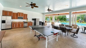 A spacious indoor area with a ping pong table, kitchen area, ceiling fans, and a view of a swimming pool. - MAIN-LAKE VIEWS Boat Slip + Community Pool-Golf Cart-Sleeps 12 (Littleton)