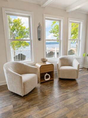 A room with two armchairs, a small wooden side table, and a view of the sea through large windows. - MAIN-LAKE VIEWS Boat Slip + Community Pool-Golf Cart-Sleeps 12 (Littleton)
