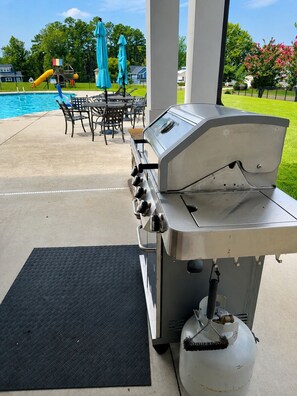 A barbecue grill with a gas tank, outdoor seating, and a pool in the background.