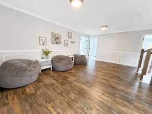 A spacious room with hardwood flooring, two bean bag chairs, a small white table with a plant, and a door leading to another room. - MAIN-LAKE VIEWS Boat Slip + Community Pool-Golf Cart-Sleeps 12 (Littleton)