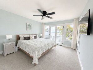 A bedroom with a bed, nightstand, lamp, ceiling fan, and a view of the outdoors through large windows. - MAIN-LAKE VIEWS Boat Slip + Community Pool-Golf Cart-Sleeps 12 (Littleton)