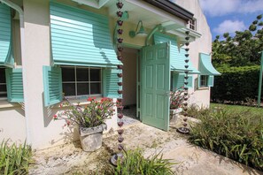 A house with a green door, a window with shutters, and a garden with plants and a bird feeder. - Cowrie Cottage | Private Pool | Near Gibbes Beach (Gibbes)