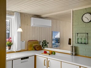 Uma cozinha moderna com armários de madeira, bancada branca, um relógio e uma janela com cortinas.
