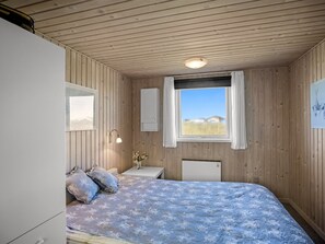 A bedroom with a bed, a bedside table, a mirror, a window, and a wall-mounted heater. - "Ingalil" - 200m from the sea by Interhome (Løkken)