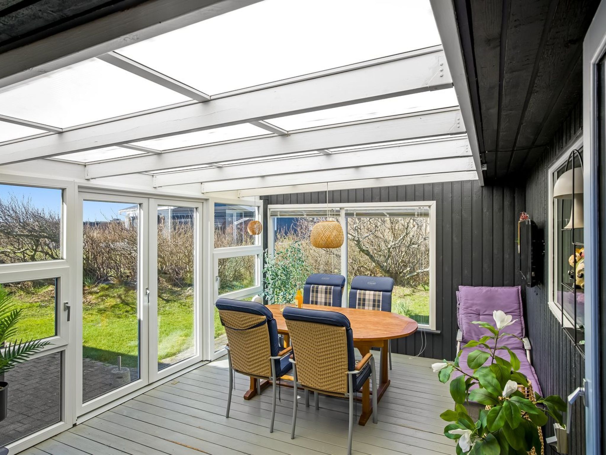 A covered outdoor dining area with a table and chairs, large windows, and a view of the outdoors.