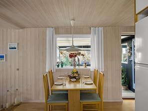 A dining area with a wooden table and chairs, a hanging light fixture, and a window with curtains. - "Ingalil" - 200m from the sea by Interhome (Løkken)