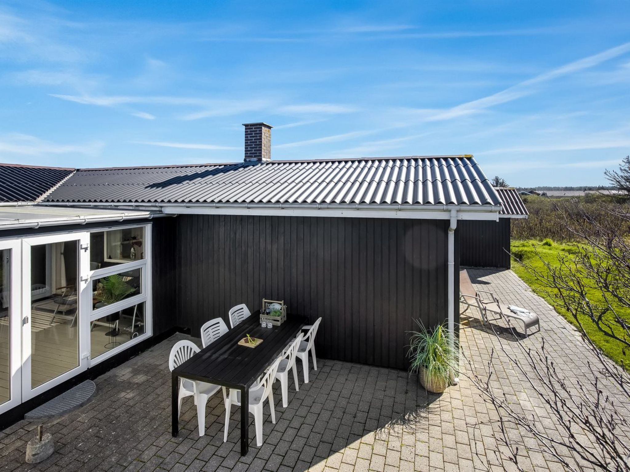Ein modernes Haus mit einer überdachten Terrasse, einem Essbereich mit Tisch und Stühlen sowie Blick auf die umliegende Landschaft.