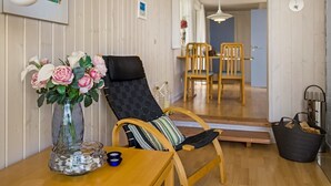 A room with a wooden table, a chair with a cushion, a vase with flowers, and a dining area with chairs and a table. - "Ingalil" - 200m from the sea by Interhome (Løkken)