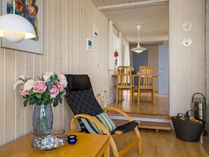 A room with a wooden table, a chair with a cushion, a vase with flowers, and a dining area with chairs and a table. - "Ingalil" - 200m from the sea by Interhome (Løkken)