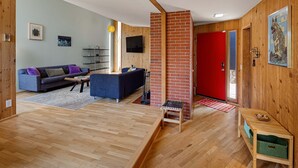 Un salon moderne avec un plancher en bois, un canapé bleu, une table basse et une porte rouge.