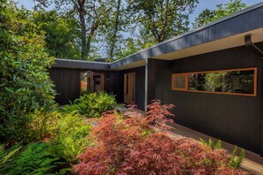 A modern house with a dark exterior, large windows, and a garden with various plants.