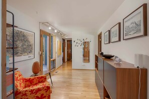 A hallway with artwork on the walls, a wooden reception desk, and a patterned chair.
