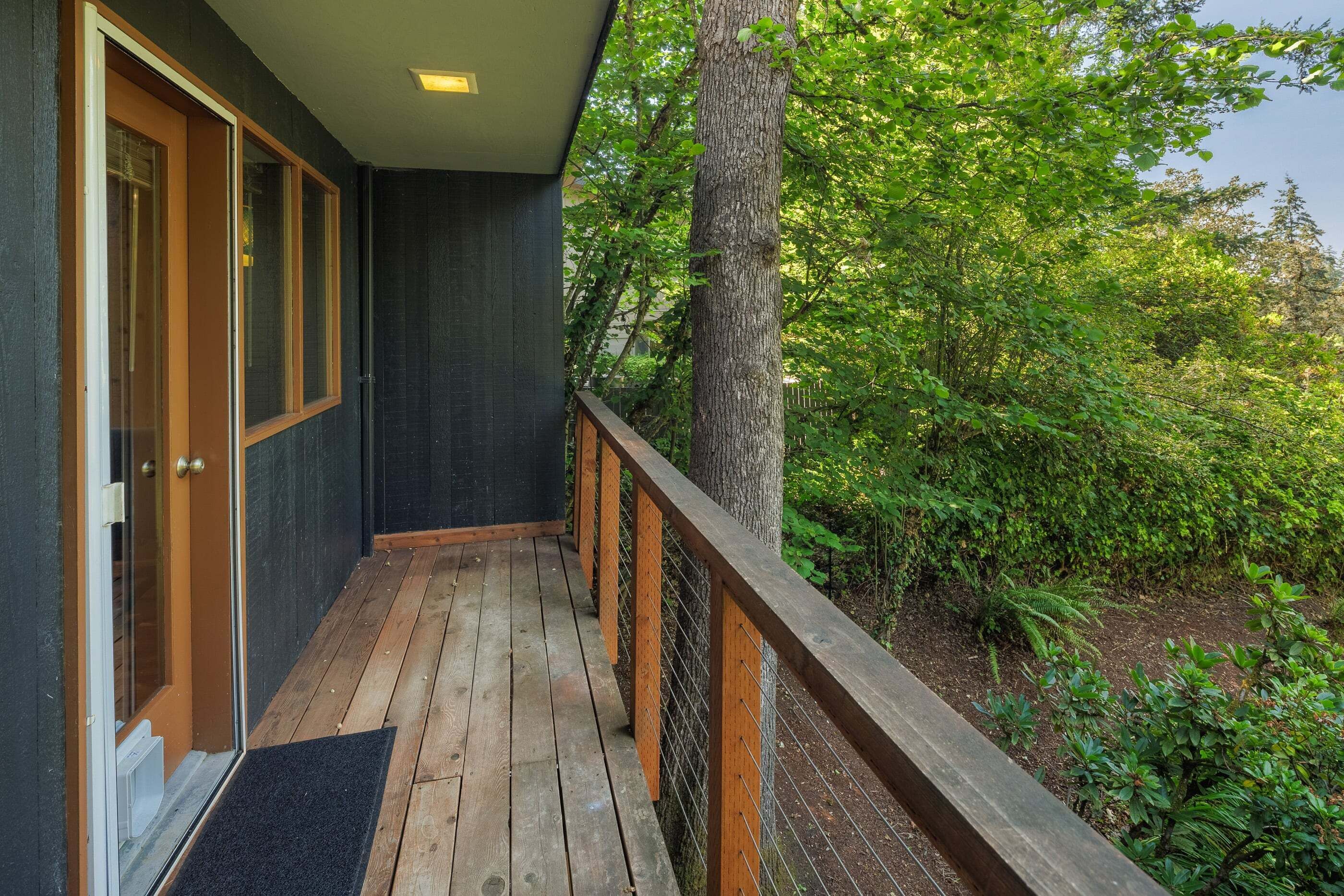 A wooden deck with a metal railing, a door, and a view of a tree-lined area.