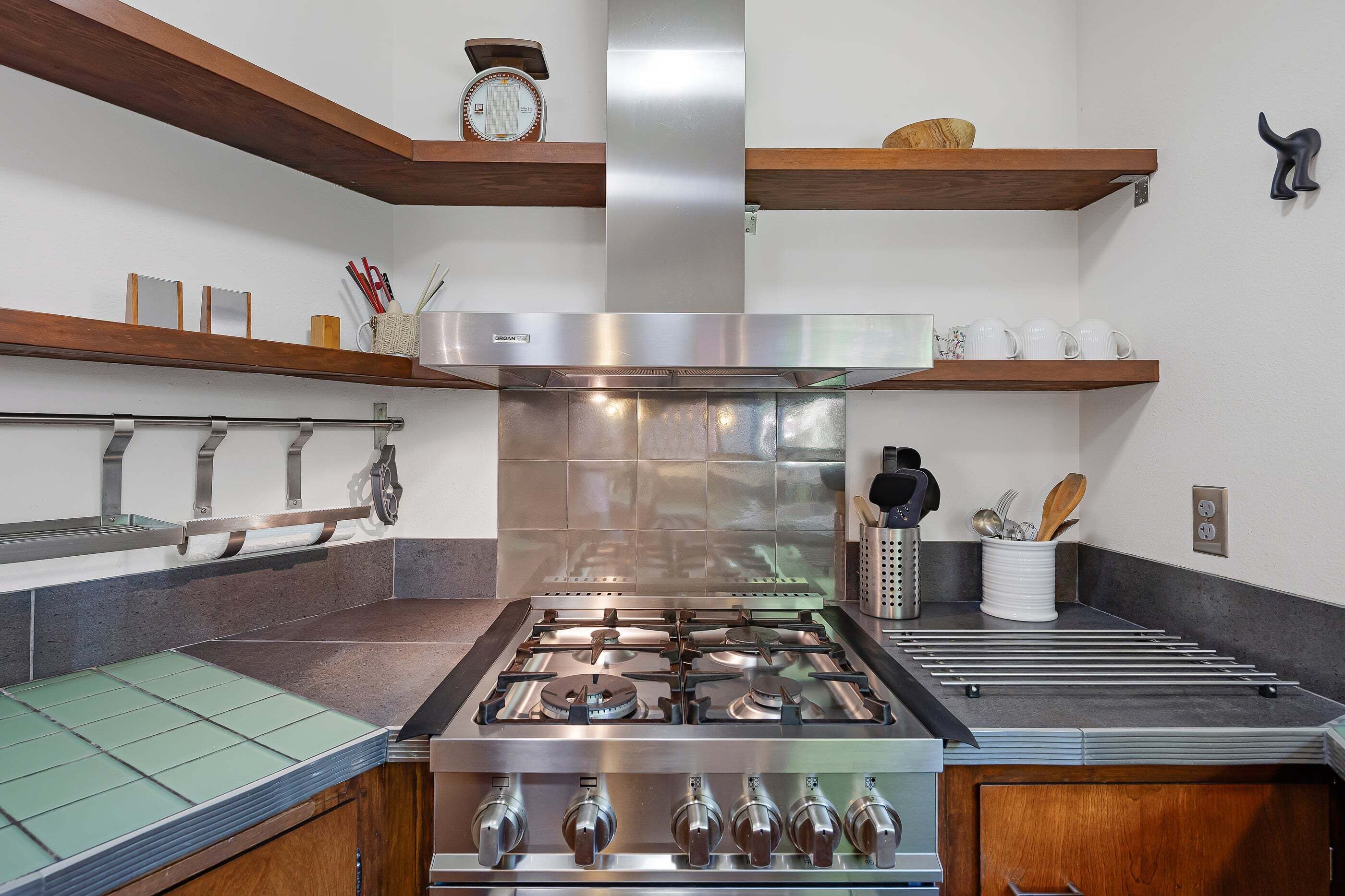 A kitchen with a stainless steel stove, wooden shelves, and a clock on the wall.