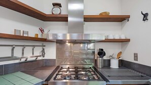 Une cuisine équipée d’une cuisinière en acier inoxydable, d’étagères en bois et d’une horloge murale.