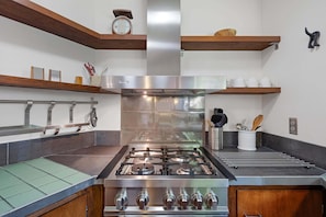 Una cocina con estufa de acero inoxidable, estantes de madera y un reloj en la pared.