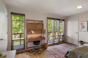 Een slaapkamer met een bureau, een stoel, een bed en grote ramen.