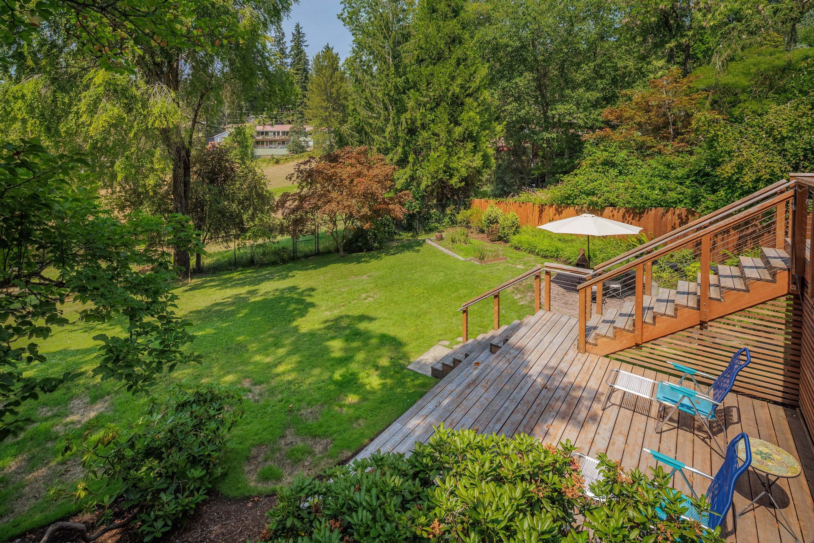 Um deck de madeira com móveis de exterior, gramado e vista para uma casa ao fundo.