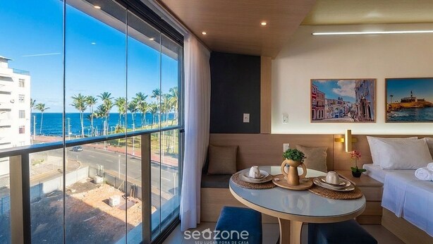 A modern hotel room with a balcony, a round table with a vase and teapot, and two paintings on the wall. - Studio in Cond. W/pool 480m the Lighthouse Spb0407 (Salvador)