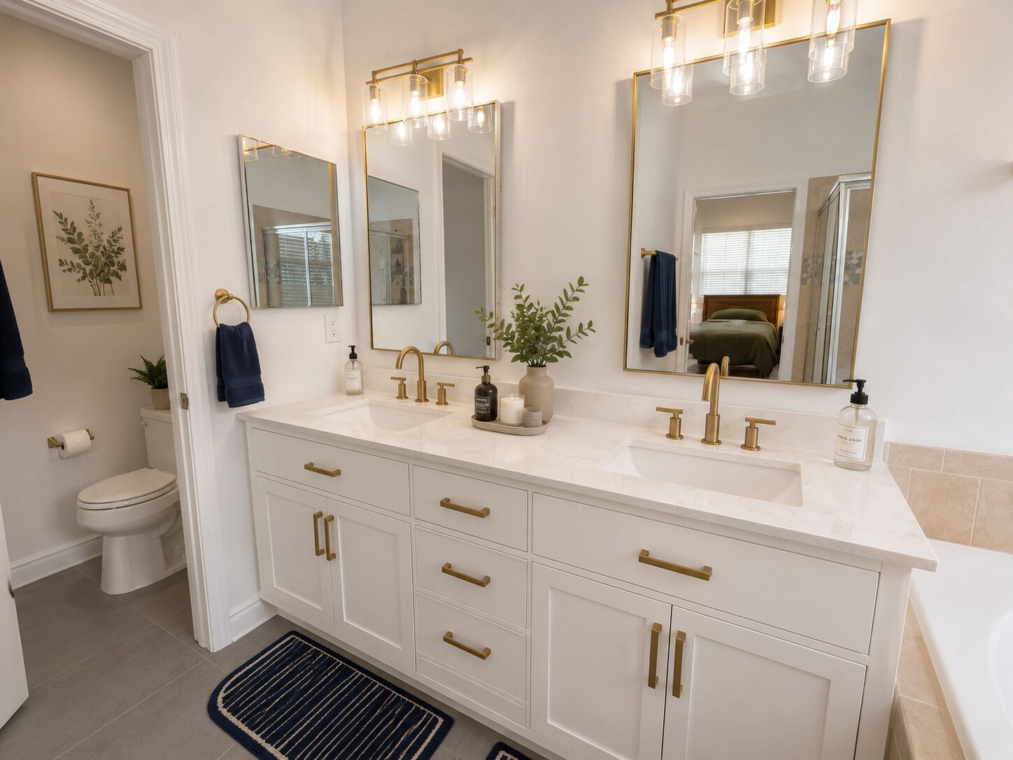 A bathroom with a white vanity, gold faucets, and a large mirror with lights.