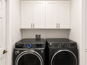 A laundry room with two front-loading washing machines, white cabinets above, and a door on the left. - Spectacular four bedroom built-in gym, built-in game room, in gorgeous Naples (Naples)