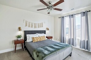 A bedroom with a bed, a ceiling fan, a nightstand, a wall-mounted lamp, and a window with curtains. - Luxury Kanab Hot Tub - Trails & Pets OK (Kanab)