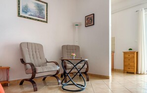 Ein Zimmer mit zwei Sesseln, einem kleinen Tisch mit einer Vase, einer Lampe und einem Holzschrank.