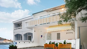 Ein zweistöckiges Gebäude mit einem Balkon, Außenbestuhlung und Pflanzkübeln.