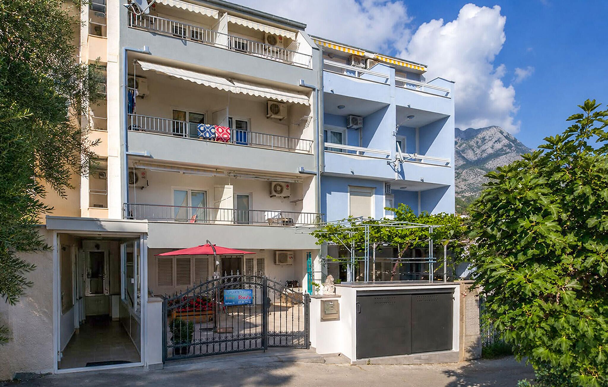 A multi-story building with balconies, a gated entrance, and a mountain view in the background.