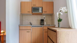 Uma cozinha compacta com armários de madeira, micro-ondas, cafeteira e uma pequena orquídea em vaso.