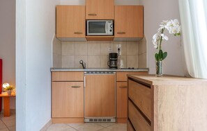 Eine kompakte Küche mit Holzschränken, einer Mikrowelle, einer Kaffeemaschine und einer kleinen Topforchidee.