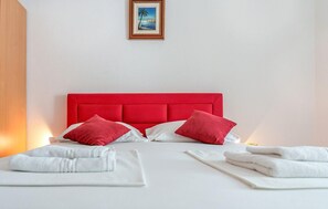 Een hotelkamer met een rood hoofdeinde, witte beddengoed en een ingelijst schilderij aan de muur.