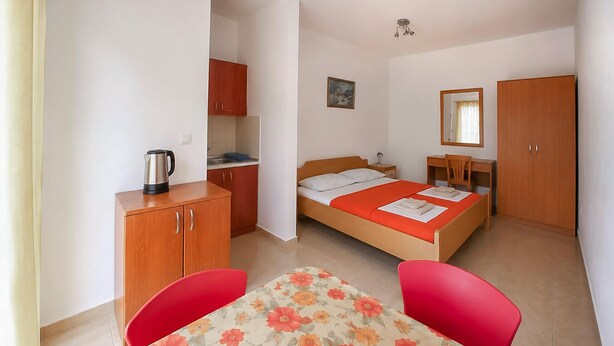 Ett kompakt hotellrum med en säng, ett skrivbord, en stol, ett litet pentry och en garderob.