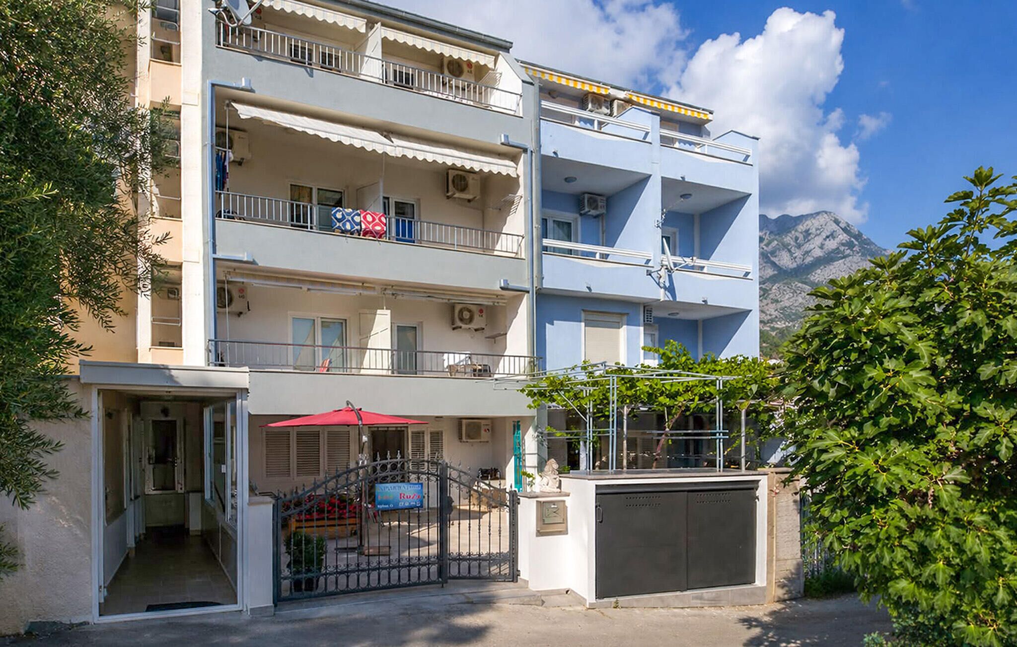 A multi-story building with balconies, a gated entrance, and a mountain view in the background.