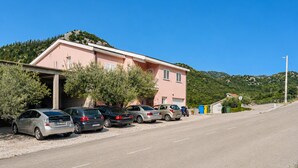 Un edificio rosa con zona de estacionamiento techada y coches aparcados al frente.