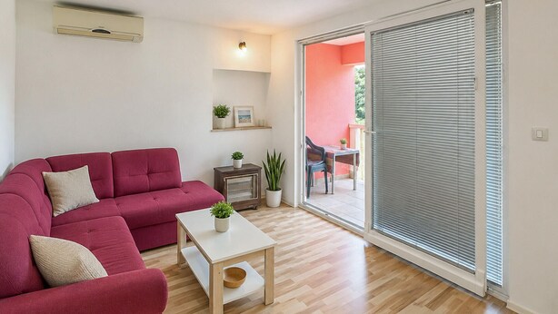 Una sala de estar con un sofá rojo, una mesita blanca y un ventanal corredero que da a un espacio exterior.