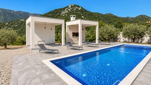 Una piscina con sillas de descanso y una pérgola, rodeada de un paisaje montañoso.