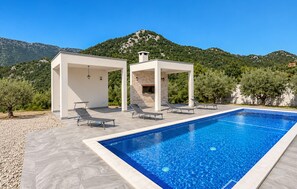 Ein Schwimmbecken mit Liegestühlen und einer Pergola, eingebettet in eine gebirgige Landschaft.