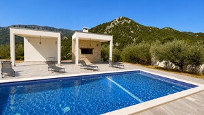 A swimming pool with lounge chairs and a pergola structure, surrounded by greenery and mountains. - 6 bedroom pet friendly apartment in Vrgorac (Vrgorac)