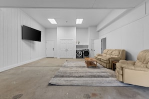 A laundry room with a washing machine, dryer, and a sofa. - Pondview Apartment at Thunder Manor (Lakewood)