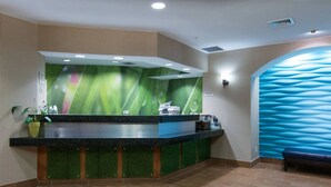 Un espace d’accueil avec une fresque murale aux tons verts et bleus, un comptoir d’accueil et un banc.