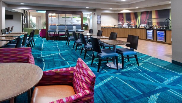 Un hall d’hôtel doté de plusieurs espaces de détente, comprenant des tables et des chaises, ainsi qu’un coin cuisine visible.