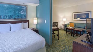 Una habitación de hotel con cama, escritorio, silla, sofá y un cuadro en la pared.